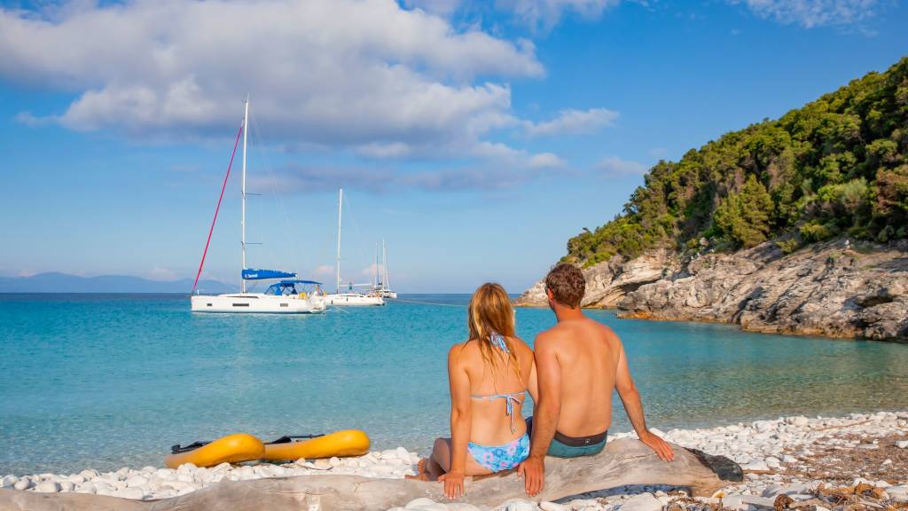 Couple sitting at the beach in Corfu Greece looking at Sunsail boats
